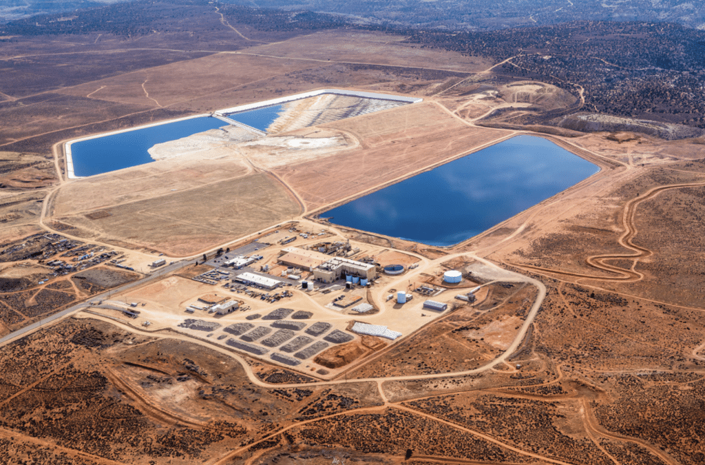 An aerial photo showing gigantic open pools filled with blue liquid, among a dry, desolate Western landscape. The entire project site has been cleared of vegetation and looks more like dirt, while trees and other brush surround the landscape.
