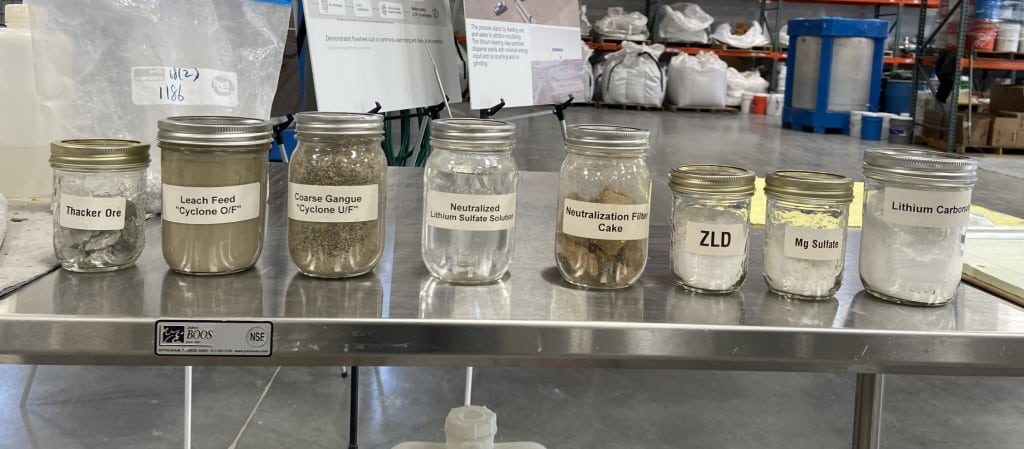 A photograph of eight glass jars on a table, showing the different phases of the lithium extraction process.